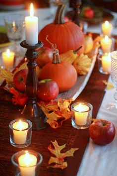 a table with candles, apples and other autumn decorations on it is set for a thanksgiving dinner