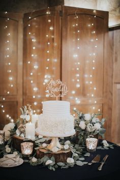 a white wedding cake sitting on top of a table next to candles and greenery