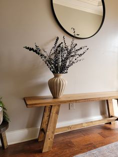 a vase with flowers sitting on a wooden bench in front of a mirror and wall