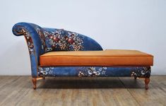 an orange and blue couch sitting on top of a hard wood floor next to a white wall