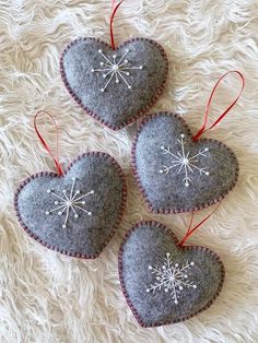 three felt heart ornaments with snowflakes hanging from them on a white furnishing