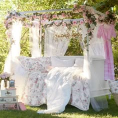 a canopy bed covered in pink and white flowers on top of a lush green field