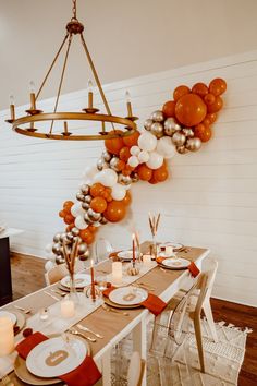 a dining room table is set with orange and white balloons hanging from the ceiling above it