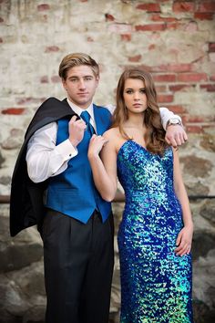 a young man and woman dressed up in formal wear posing for a photo with a brick wall behind them