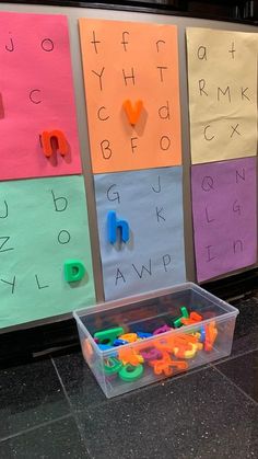 a plastic container filled with letters sitting on top of a floor next to a wall