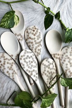 six white spoons are lined up next to each other with green leaves on them