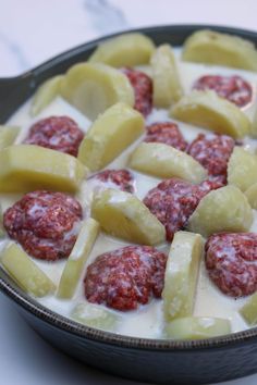 a pan filled with meatballs and potatoes covered in white sauce on top of a table