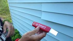 a person holding a red and white object in front of a blue house with grass