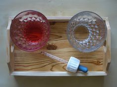 two glasses and a whisk are sitting on a wooden tray, one is empty