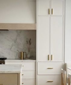 a white kitchen with marble counter tops and cabinets in the backround, next to a stove top oven