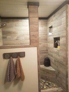 a bathroom with wooden walls and tile flooring on the shower wall, along with two towels hanging from hooks