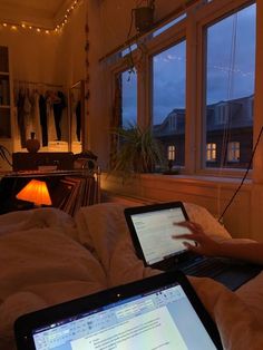 a person sitting on a bed using a laptop computer in front of a window at night