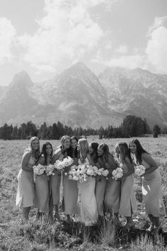 a group of women standing next to each other in a field with mountains in the background