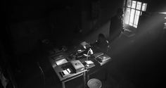 two people are standing in the dark near a desk with papers and pens on it