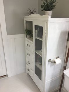 a white cabinet sitting in the corner of a room next to a toilet paper roll