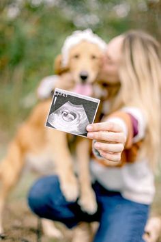 a woman holding up a photo with a dog behind her and another dog in the background