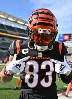 a football player wearing an orange and black uniform holding his hands together while standing on the field