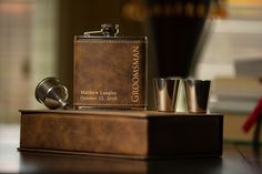 a flask and shot glasses are sitting on a table next to a leather hip flask