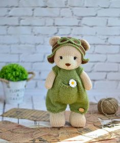 a teddy bear with a green outfit and flower in its hand on a table next to a potted plant