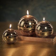 three decorative candles sitting on top of a wooden tray with gold foiled balls around them