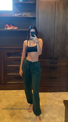 a woman taking a selfie in front of a tv wearing green pants and crop top