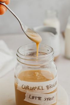 a spoon full of caramel sauce being poured into a jar with labels on it