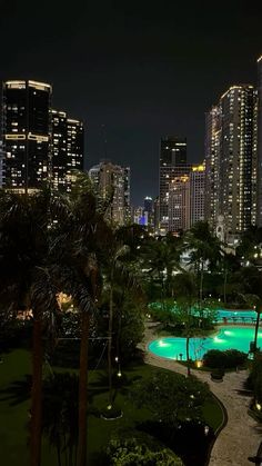 the city skyline is lit up at night with lights reflecting in the pool and palm trees