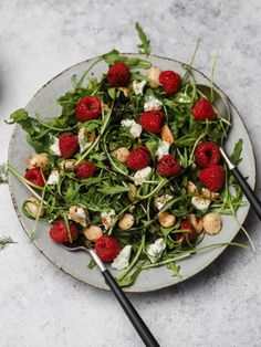 a salad with strawberries and goat cheese is on a plate next to some chopsticks