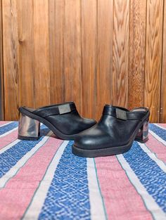 Elevate your shoe game with these stunning vintage Clash leather clogs, a true testament to 90s fashion. Designed with a bold, chunky heel and sleek black leather, these clogs are perfect for anyone looking to add a touch of edgy sophistication to their wardrobe. Key Features: Brand: Clash Era: 1990s, Made in Spain Material: Genuine leather upper with sturdy synthetic sole Color: Classic black with a metallic silver block heel Size: UK 5 (Approx. EU 38, US 7) Insole: 24cm Heel Height: 9cm Striki Black Clogs With Sculpted High Heel, Black Closed Toe Clogs With Sculpted Heel, Retro Closed Toe Leather Mules, Black Leather Clogs With Sculpted Heel, Retro Leather Platform Mules, Retro Leather Closed Toe Mules, Modern Black Clogs With Sculpted Heel, Modern Clogs With Padded Heel, Modern Clogs With Padded Heel And Round Toe