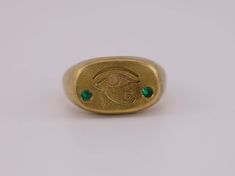 The iconic symbol of the Eye of Horus, revered for its protective powers, is boldly engraved on the cushion signet face. Flanking the eye are two brilliant lab-grown emeralds, reminiscent of the lush beauty of ancient Egypt. This ring is a masterful blend of historic symbolism and modern sophistication, designed with an aged brush finish 22k gold vermeil. Made in solid sterling silver, this ring is a weighty piece. Discover a piece that connects the mystic past with the brilliant present. This piece is made to order, so please allow approximately 3 weeks for the craftsmanship required. Alternative stone options available - please reach out for more info. Instagram - @caeliajewellery Website - www.caeliajewellery.com/ Symbolic Oval Engraved Ring For Ceremonial Occasions, Symbolic Oval Etched Signet Ring, Symbolic Etched Oval Signet Ring, Gold Engraved Emerald Ring Gift, Symbolic Etched Signet Ring, Engraved Gold Emerald Ring As A Gift, Symbolic Etched Oval Engraved Ring, Symbolic 14k Stamped Engraved Ring, The Eye Of Horus