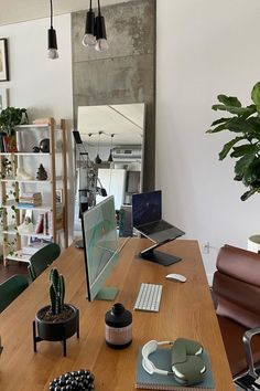 a wooden table topped with computer monitors and laptops next to a potted plant