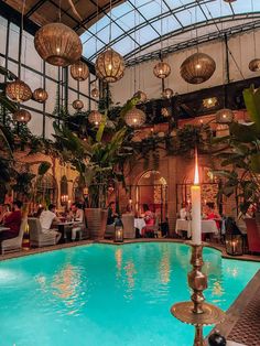 an indoor swimming pool with lights hanging from the ceiling and people sitting at tables around it