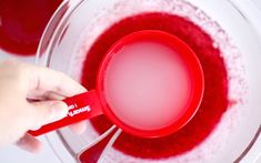 a person is mixing red liquid in a bowl with a measuring spoon on the side