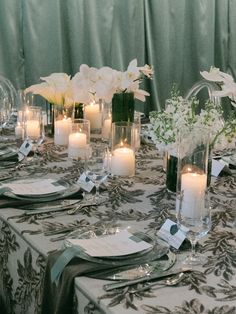 the table is set with white flowers, candles and place settings for an elegant dinner