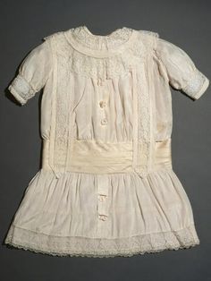 an old white dress with lace on the bottom and collar, is hanging up against a gray wall