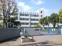 an industrial building with trees in the foreground and fenced off area to the side