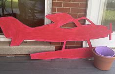 a red airplane sitting on the front porch next to a flower pot and window sill