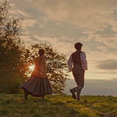 two people are walking in the grass at sunset