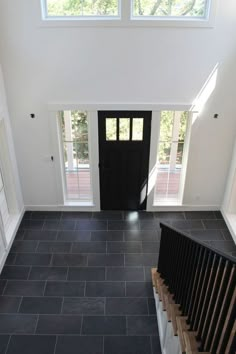 an overhead view of a black door and stairs in a white room with two windows