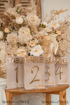 the table numbers are on display in front of a bouquet of white and gold flowers