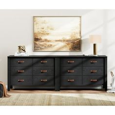 a black dresser with gold handles in a white living room, next to a painting on the wall