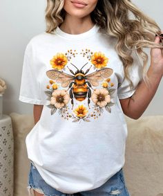 Embrace nature's beauty with our "Floral Bee Shirt," a stunning piece of wearable art that celebrates the enchanting world of pollinators. This Botanical tee features a vivid depiction of a bee amidst a flourish of wildflowers, designed for those who cherish the outdoors and the vital role of bees in our ecosystem. Perfect for garden lovers and bee enthusiasts alike, it's more than just clothing--it's a statement of love and support for our natural world. Crafted with eco-friendly materials, thi Nature-inspired Crew Neck T-shirt For Summer, Summer Nature-inspired Crew Neck T-shirt, Nature-inspired Short Sleeve T-shirt For Summer, Crew Neck T-shirt With Plants Print, Plants Print Crew Neck T-shirt Gift, Plants Print Crew Neck T-shirt For Gift, Spring Botanical Graphic Print T-shirt, Cottagecore Tshirt, Spring Cottagecore Printed T-shirt