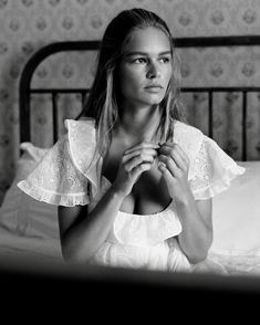 a woman sitting on top of a bed holding her hands up in front of her chest