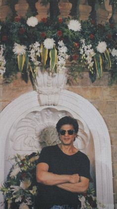 a man wearing sunglasses standing in front of a white arch with flowers and foliage on it