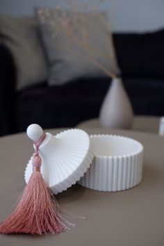 a white vase with a pink tassel sitting on top of a table next to a cup