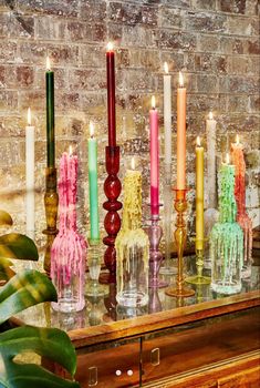 there are many different colored candles in the vases on the table and behind them is a brick wall