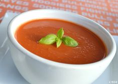 a white bowl filled with tomato soup and garnished with green leaves on top