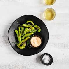 some green peppers on a black plate with dipping sauce