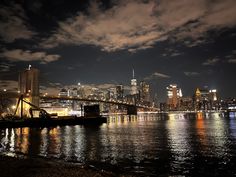 the city skyline is lit up at night with clouds in the sky and lights reflecting on the water