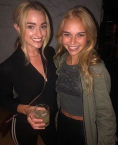 two beautiful young women standing next to each other holding glasses in front of the camera